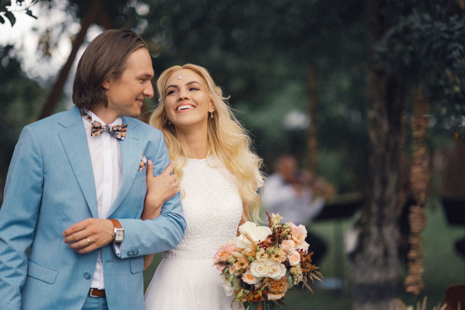 A couple shares a tender moment under trees at their outdoor wedding.