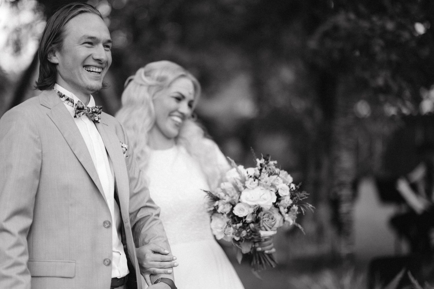 A black and white portrait of a newlywed couple laughing together outdoors.