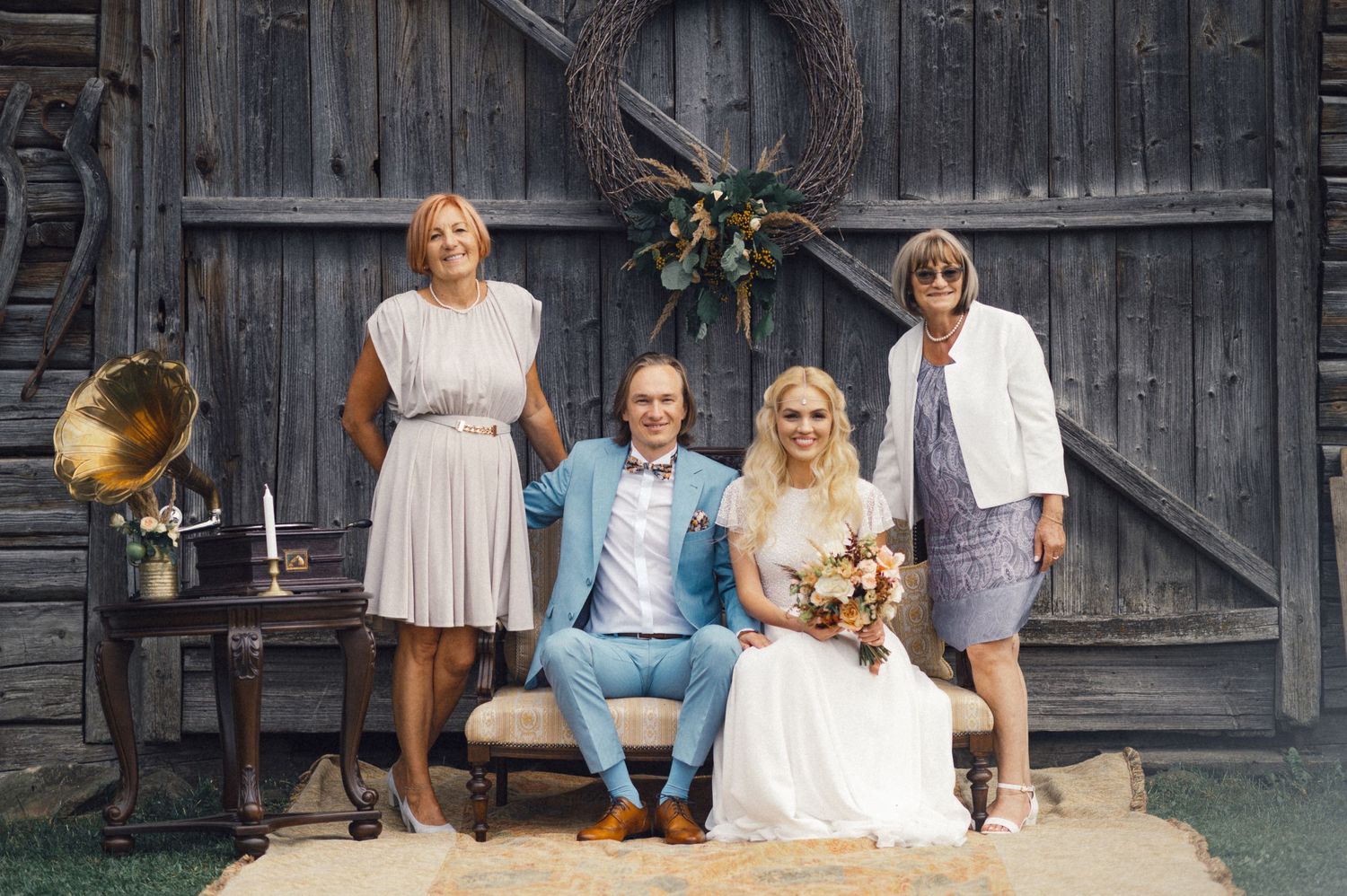 A wedding party poses together on wooden steps in front of a rustic barn door.
