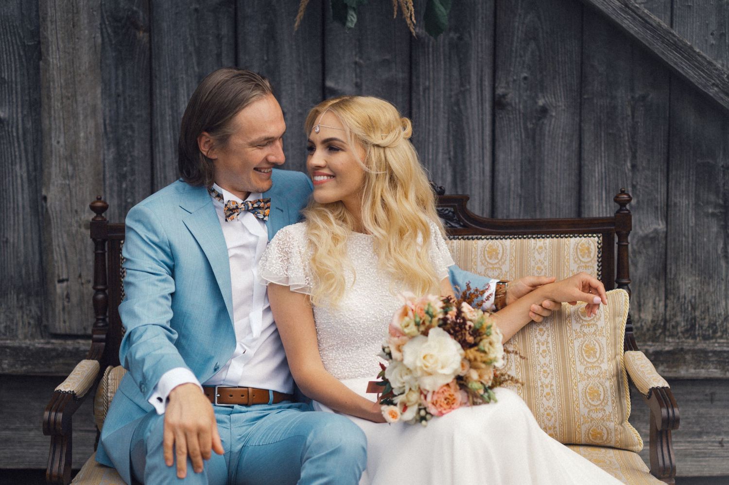 A couple in light blue and white share an intimate moment on a vintage bench.