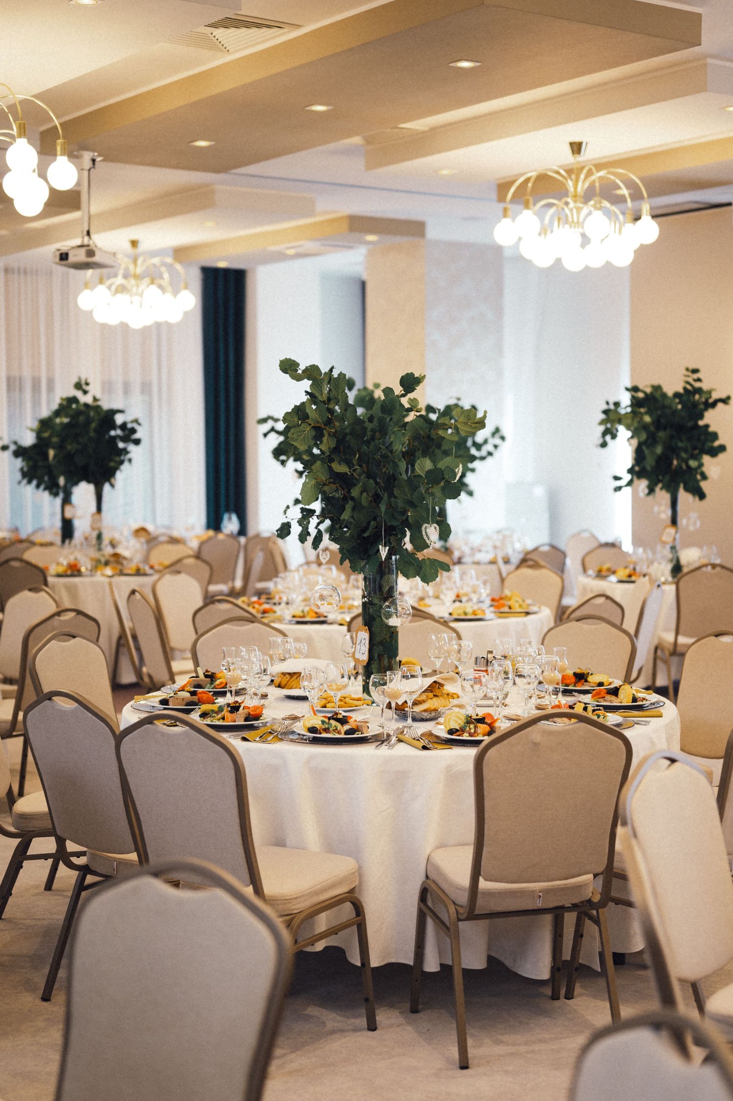 Formal wedding reception venue with elegant chandeliers and round tables set for dining.
