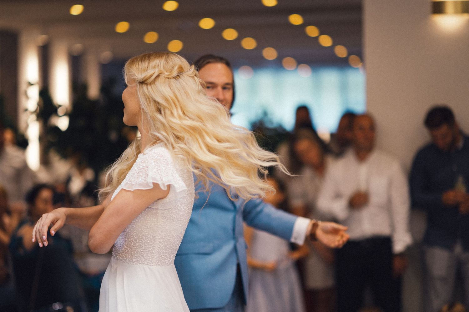 Couple performing energetic dance moves during wedding reception with guests watching.