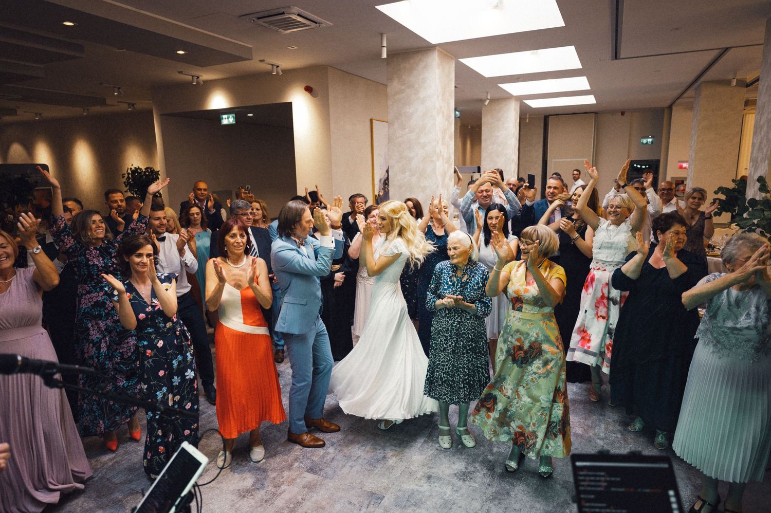 Large group of wedding guests celebrating and dancing together in an indoor venue.