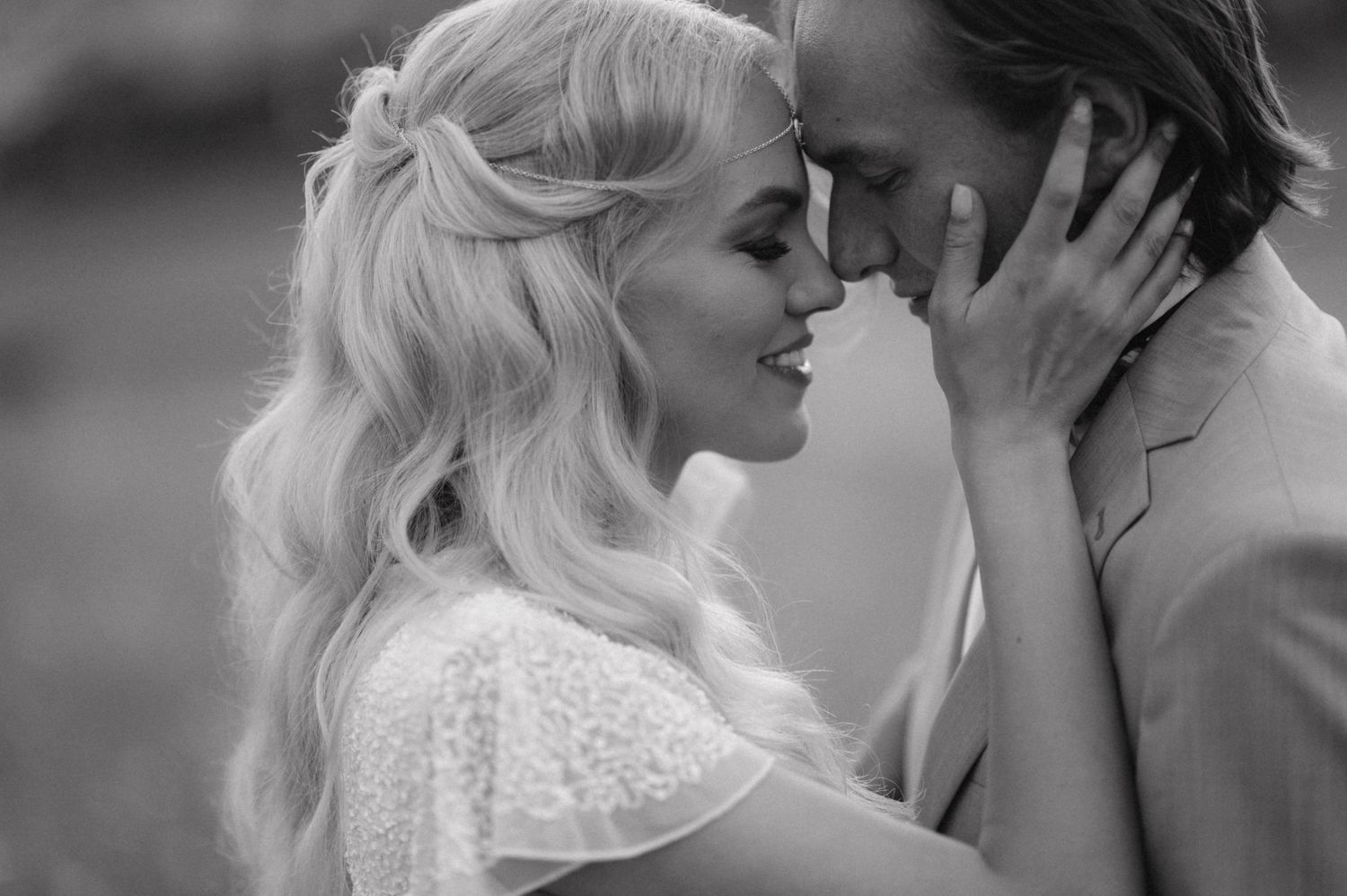 Black and white photo of intimate couple sharing tender moment against blurred background.