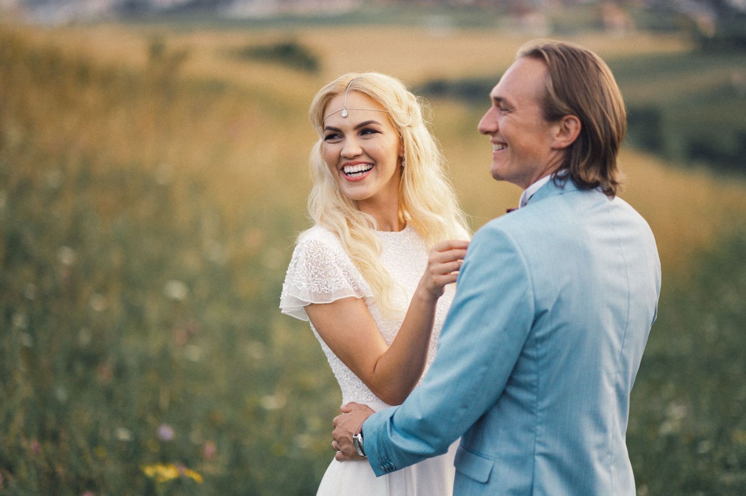 Joyful couple sharing laughter in sunny meadow wearing formal attire.
