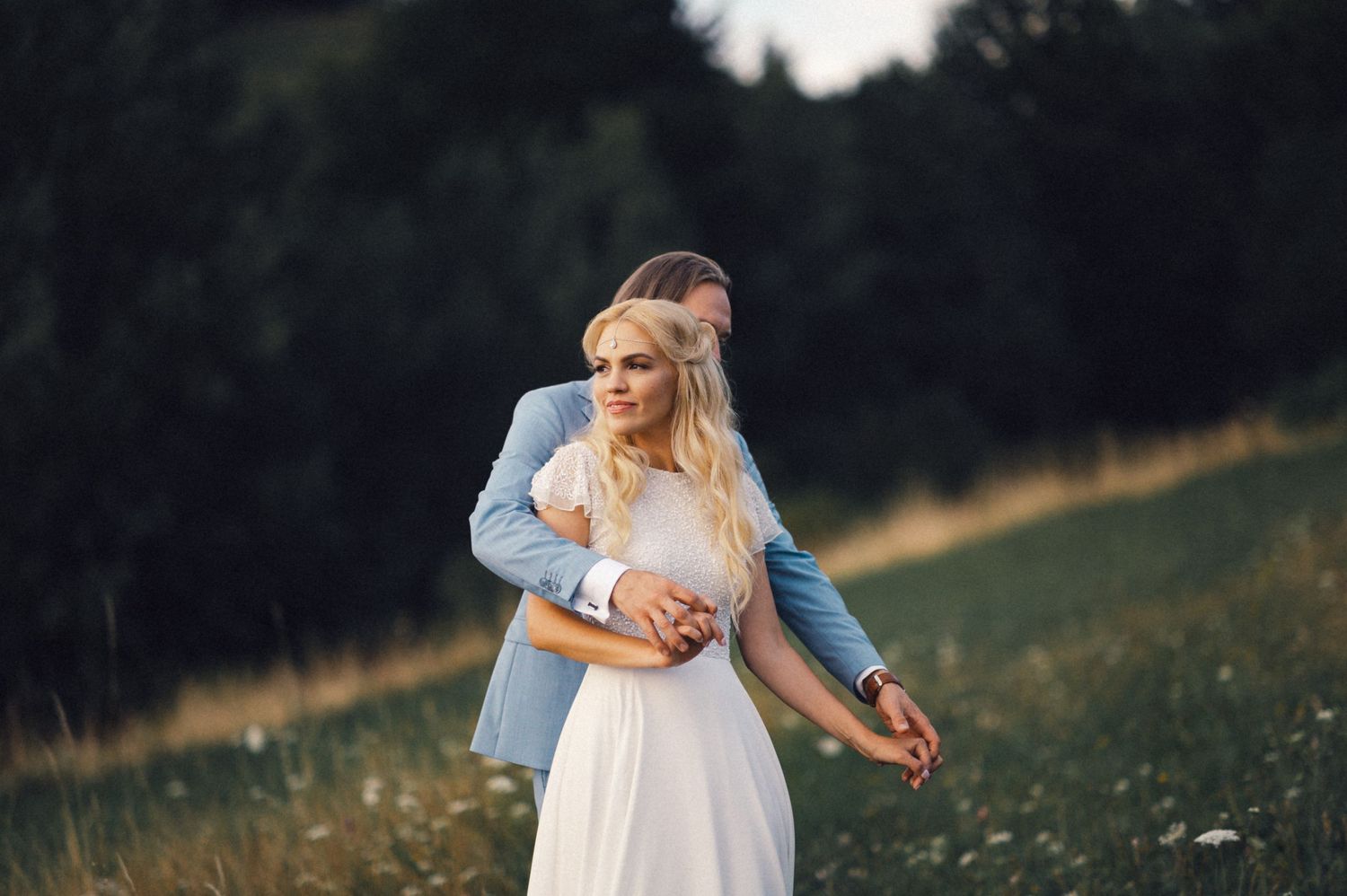 Couple in romantic embrace standing in wildflower meadow at golden hour.