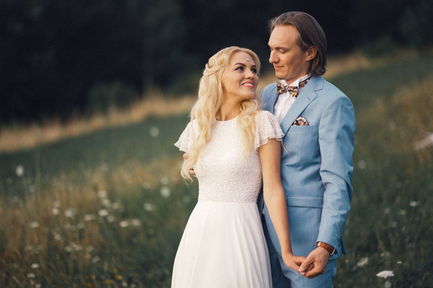 Romantic couple in formal attire standing close in sunlit wildflower field.