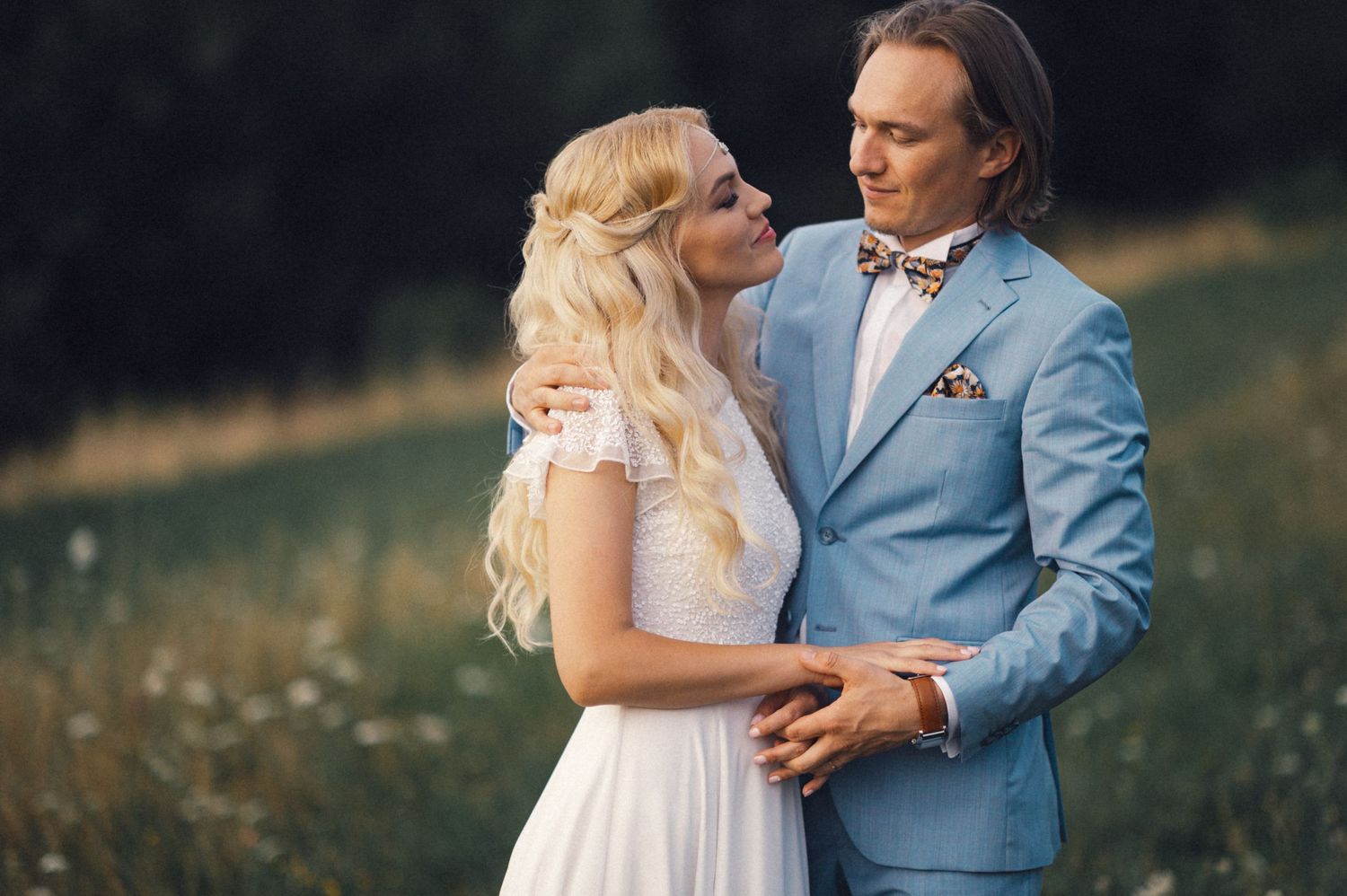 Elegant couple in formal wear sharing intimate moment in flowering meadow.