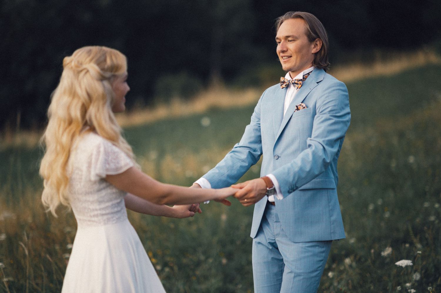 Couple holding hands and dancing together in summer meadow wearing formal attire.
