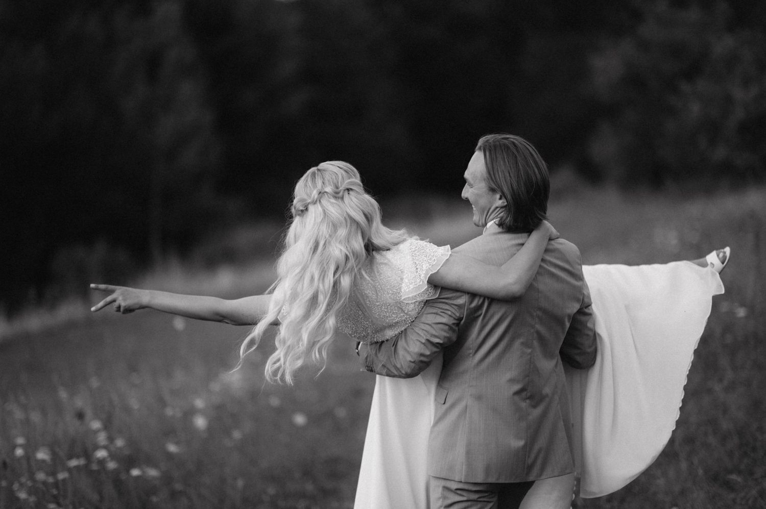 A black and white photo captures a romantic embrace between a couple in formal attire on a grassy hillside.