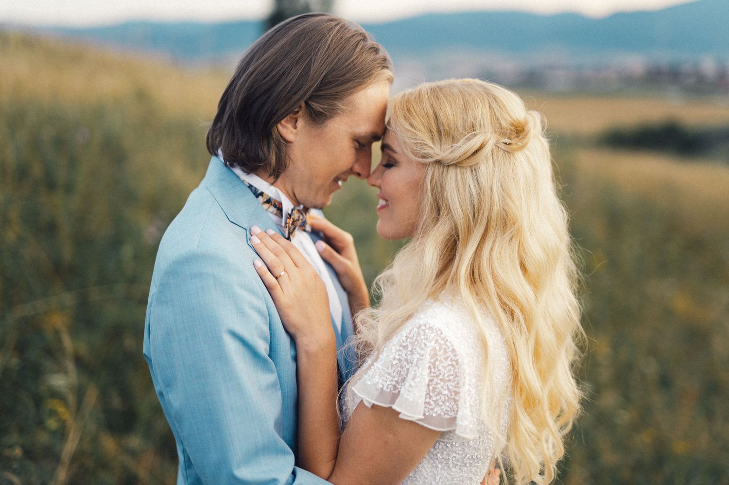 A couple shares a tender close-up moment in a meadow wearing coordinated light blue and white outfits.