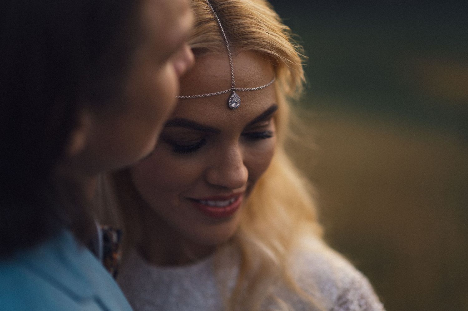 Close-up shot of a bride wearing a delicate forehead jewelry piece during an outdoor wedding ceremony.