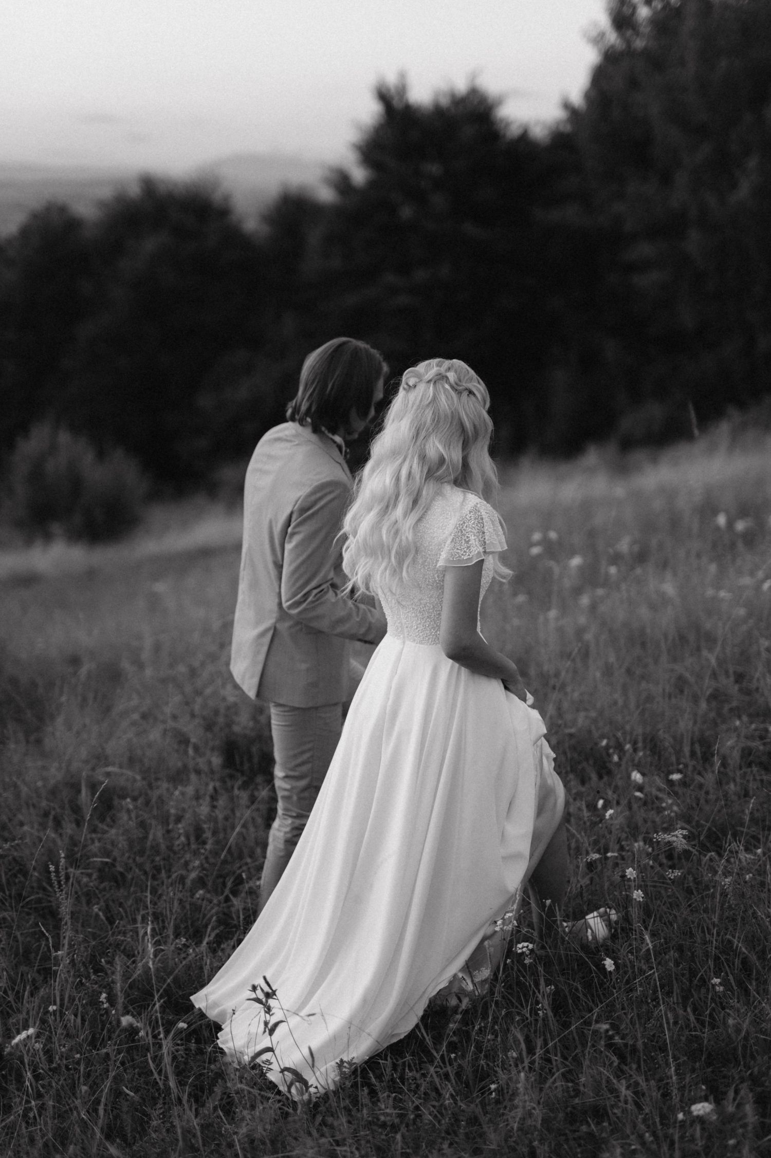 Black and white portrait of newlyweds standing in a wildflower meadow at dusk.