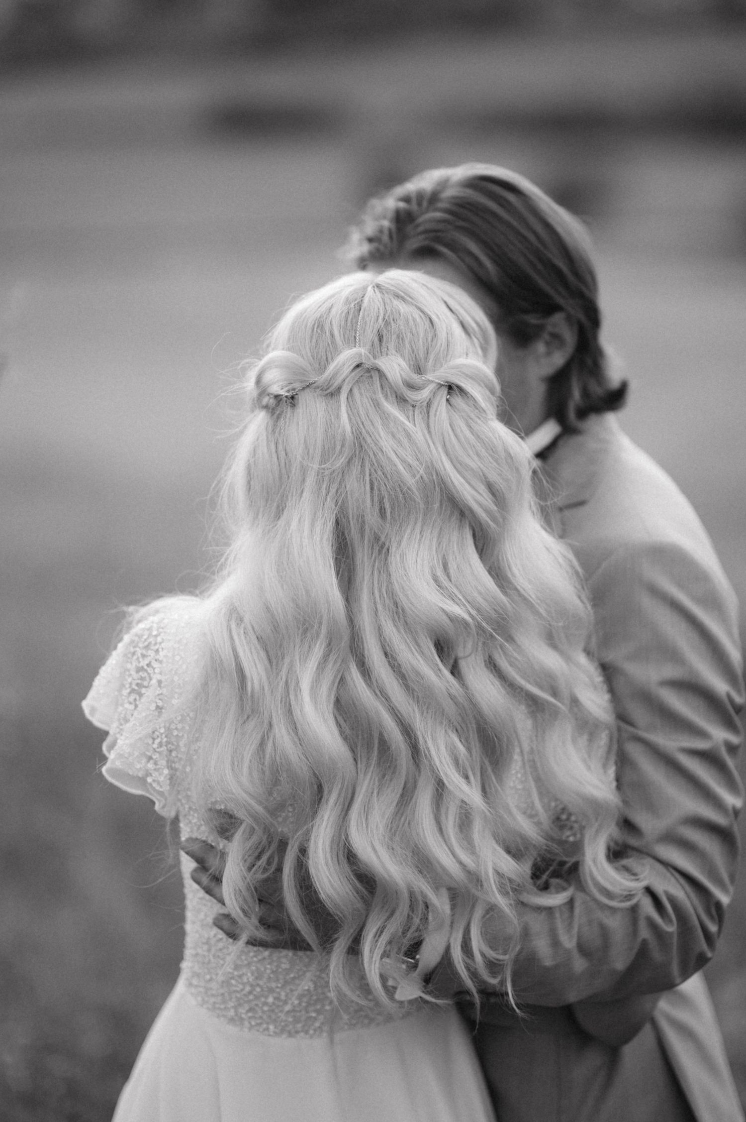 Black and white portrait showing bride's long wavy hair with braided crown detail.