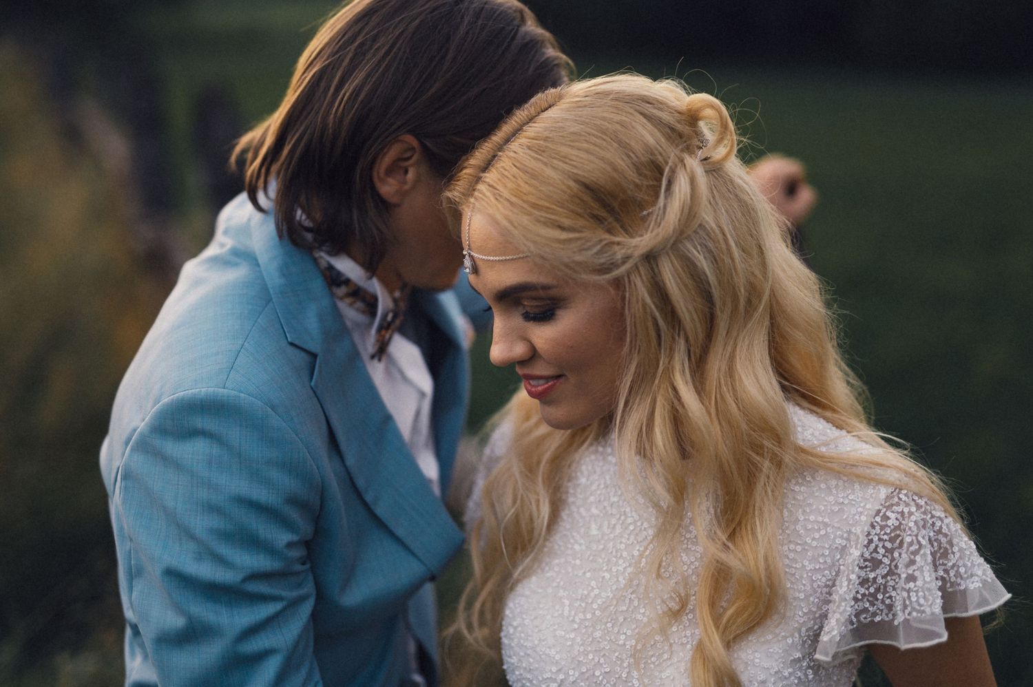 Intimate wedding portrait of couple in blue suit and lace dress against natural background.