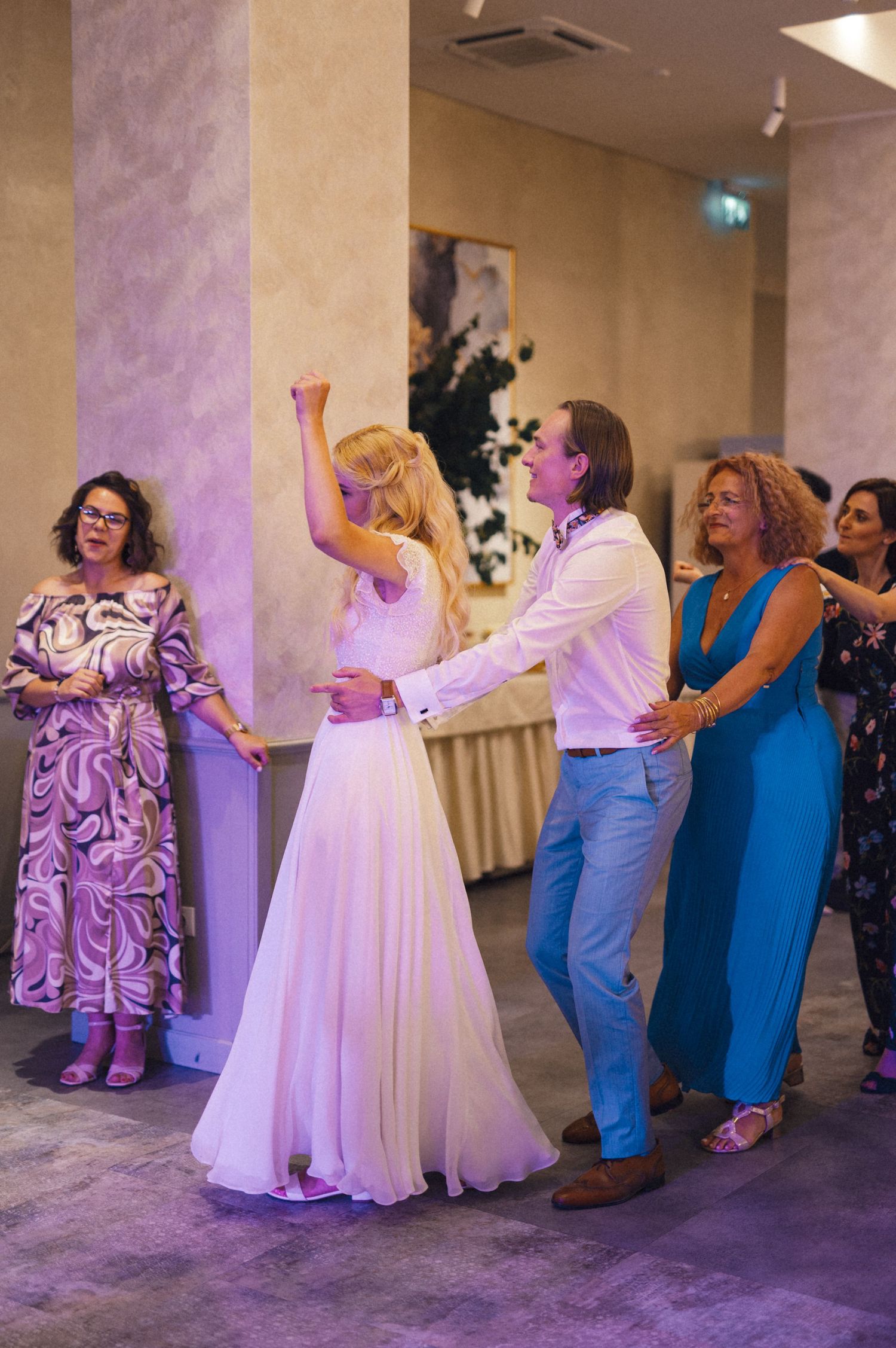 Wedding guests dancing and celebrating at a reception with purple lighting.