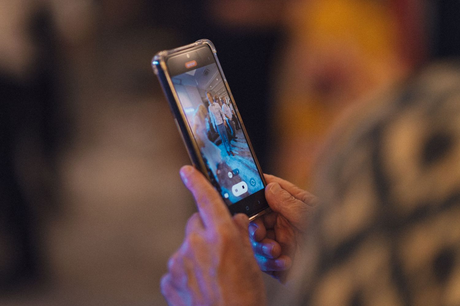 Someone holding a phone displaying a photo at an event with blue lighting.