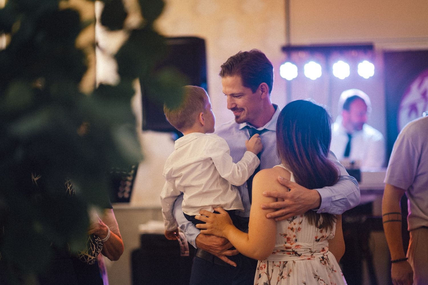 Family dancing together at a wedding reception with stage lights in background.