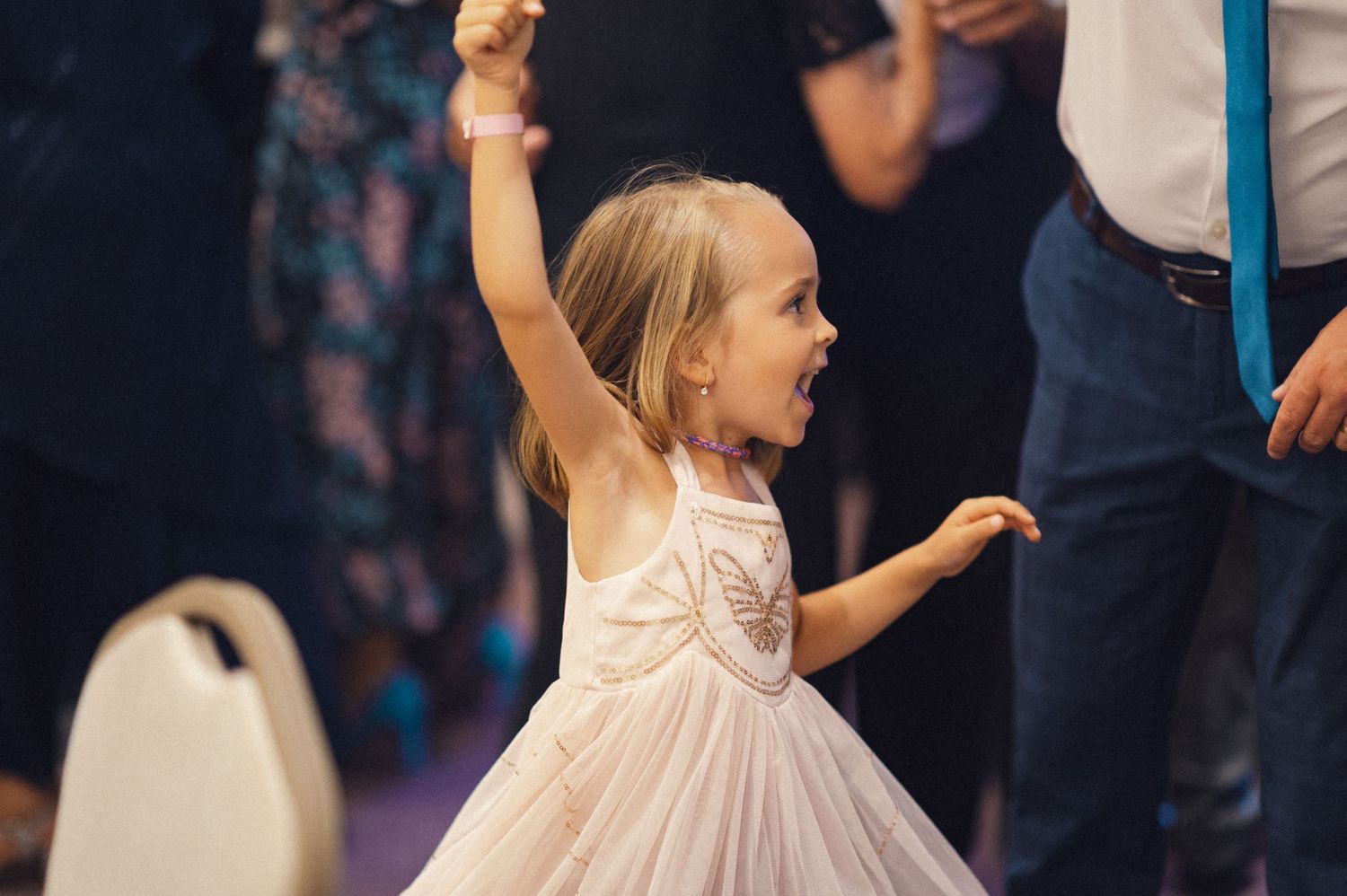 Young girl in a white dress twirls joyfully on the dance floor at a celebration.
