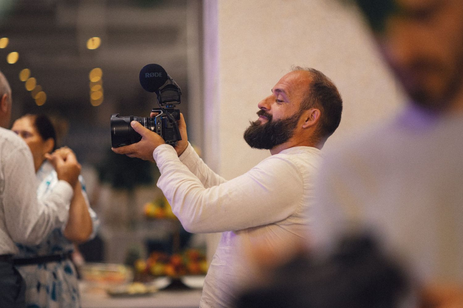 Bearded photographer holding a professional camera captures moments at an event.