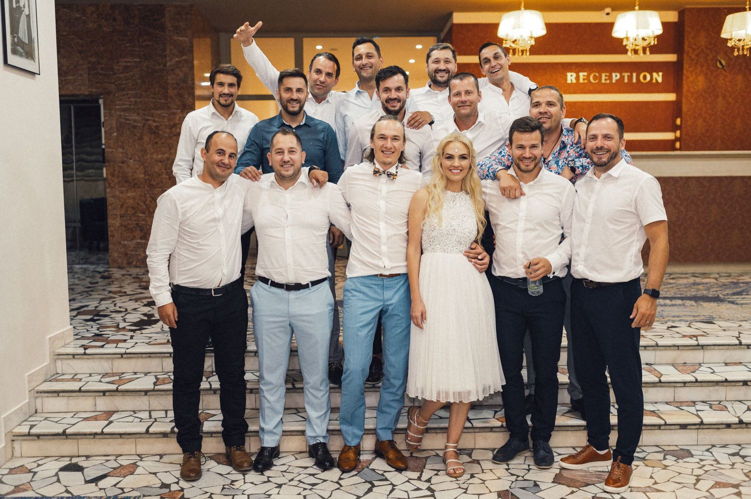 Group photo of wedding party members posing on stone steps outside a reception venue.