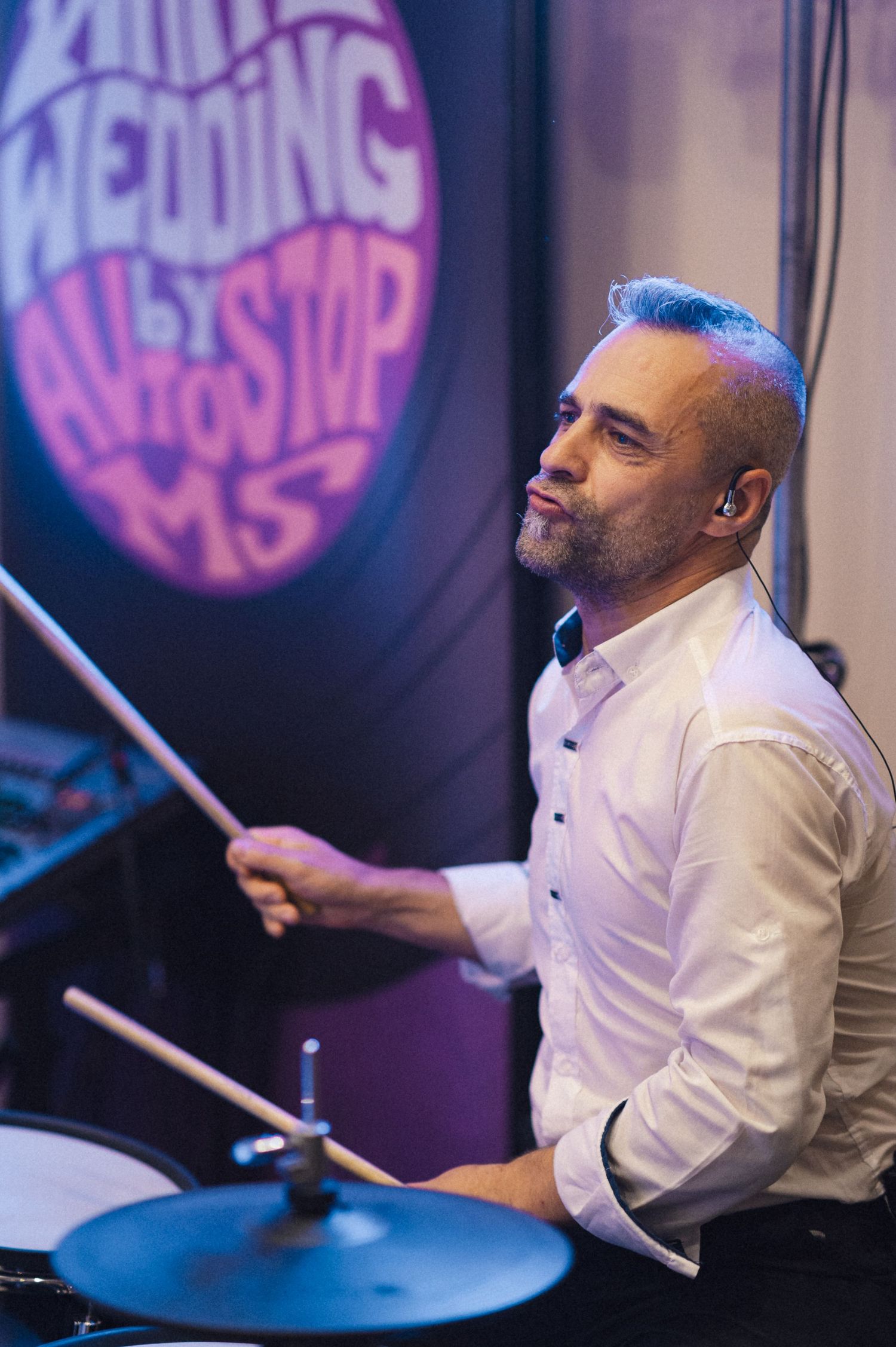 Wedding band drummer performing in front of a neon sign at reception.