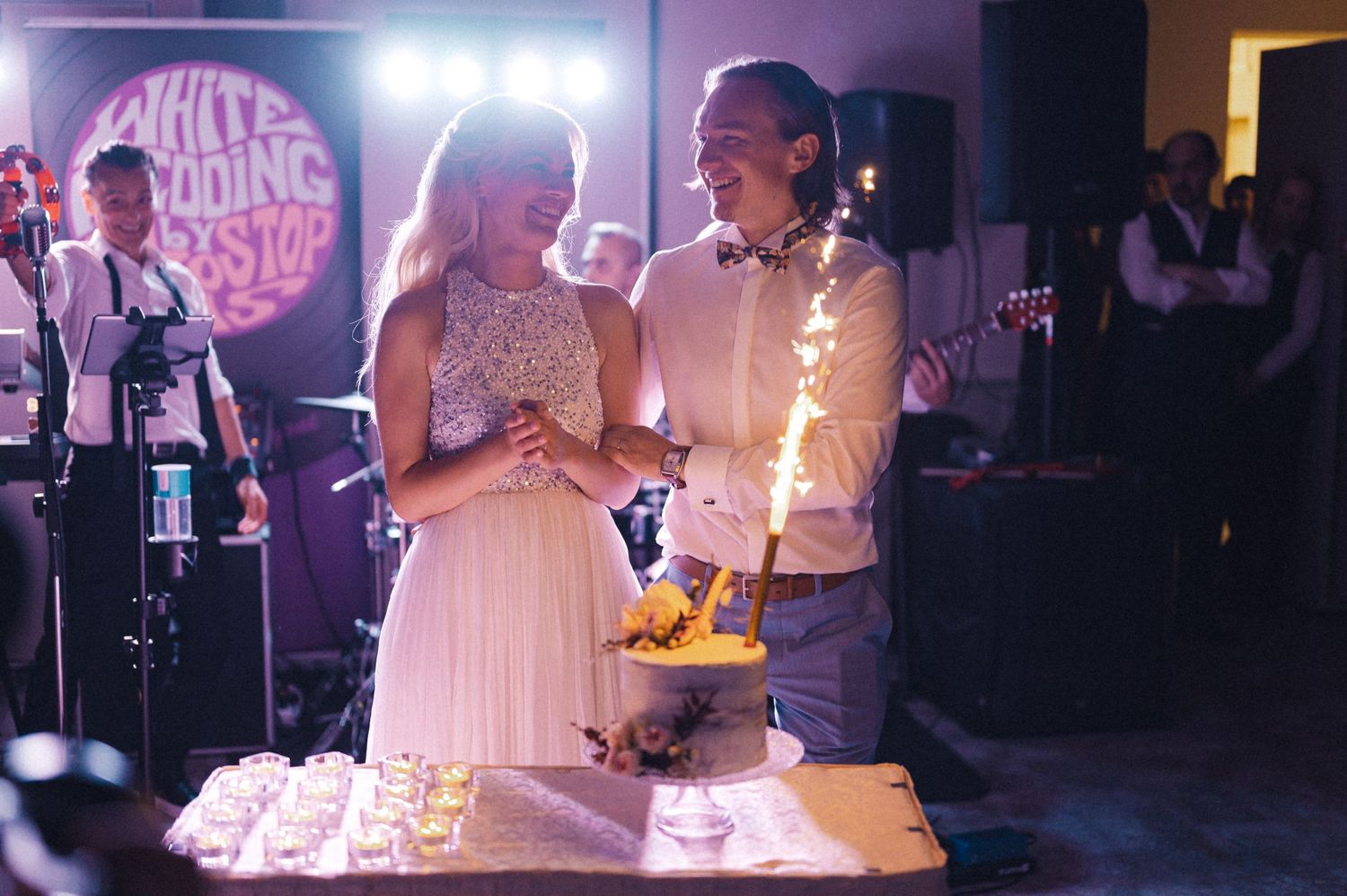 Couple cutting wedding cake with sparklers at dimly lit reception.