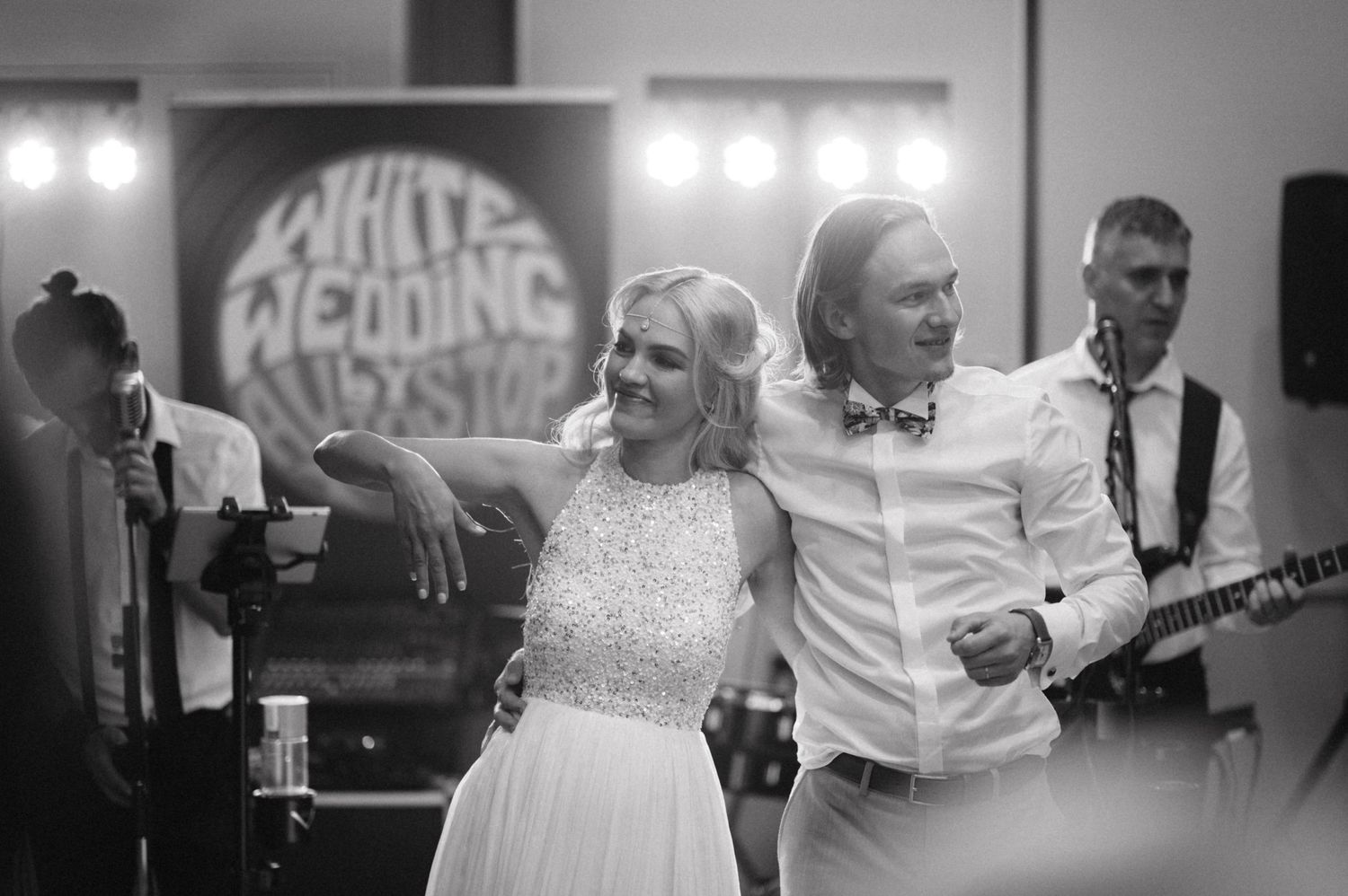 A couple dances together at their wedding reception with a live band performing in the background.
