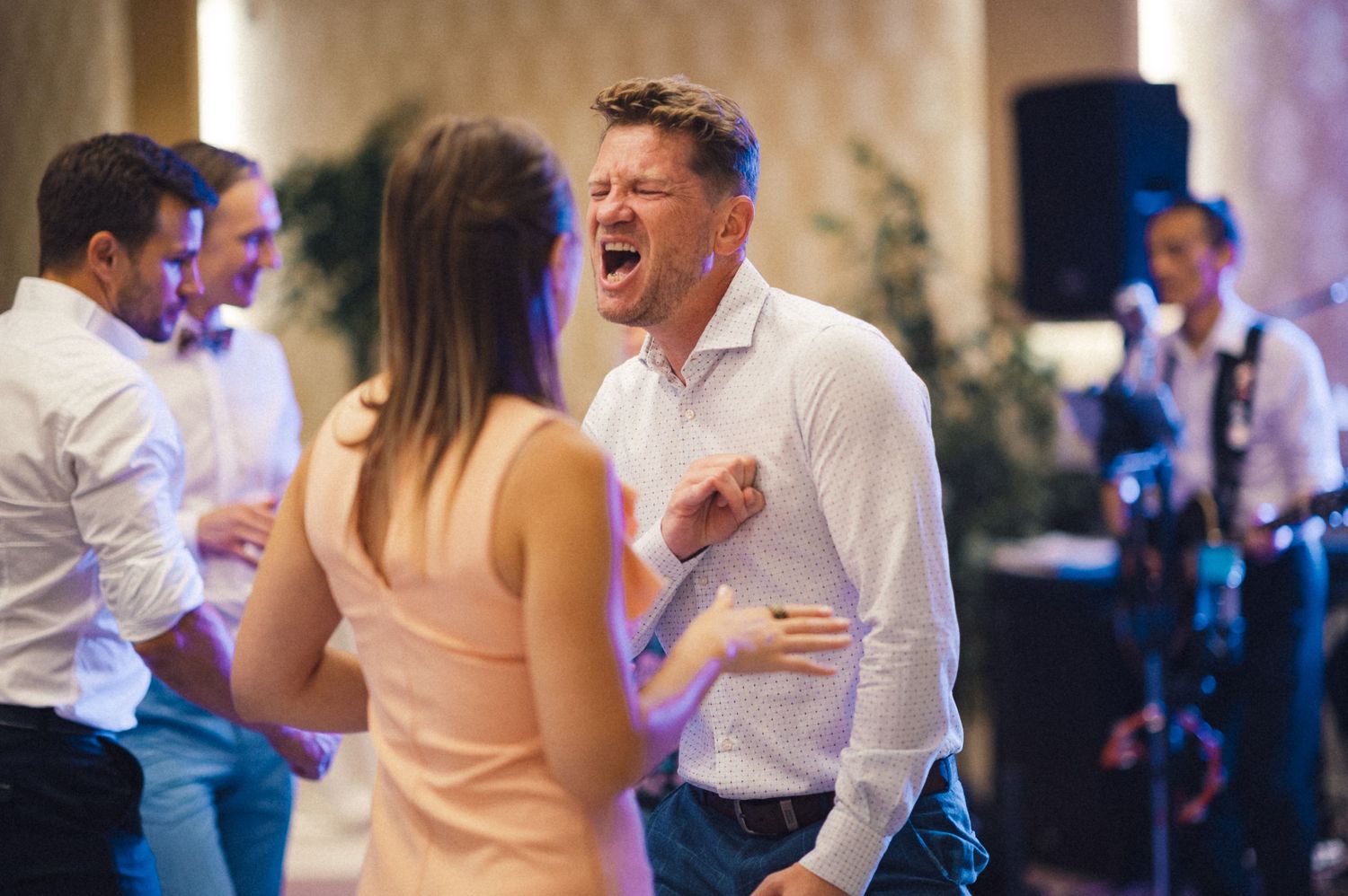 Guests dancing and celebrating energetically at a wedding reception with band in background.