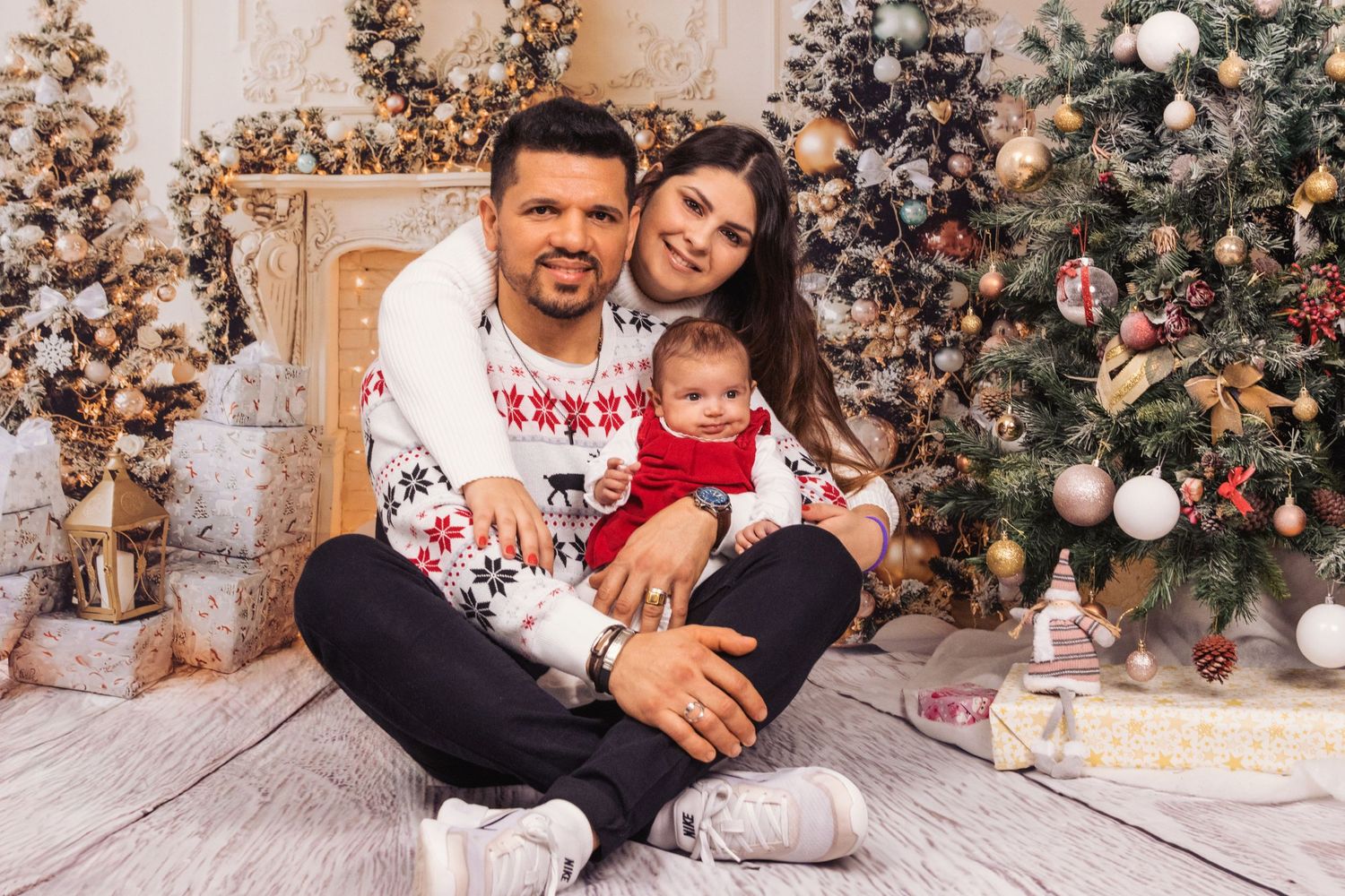 A festive family portrait in front of decorated Christmas trees with white and silver ornaments.