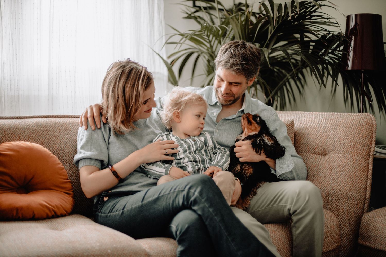 An intimate living room scene with people cuddling on a grey couch near houseplants.