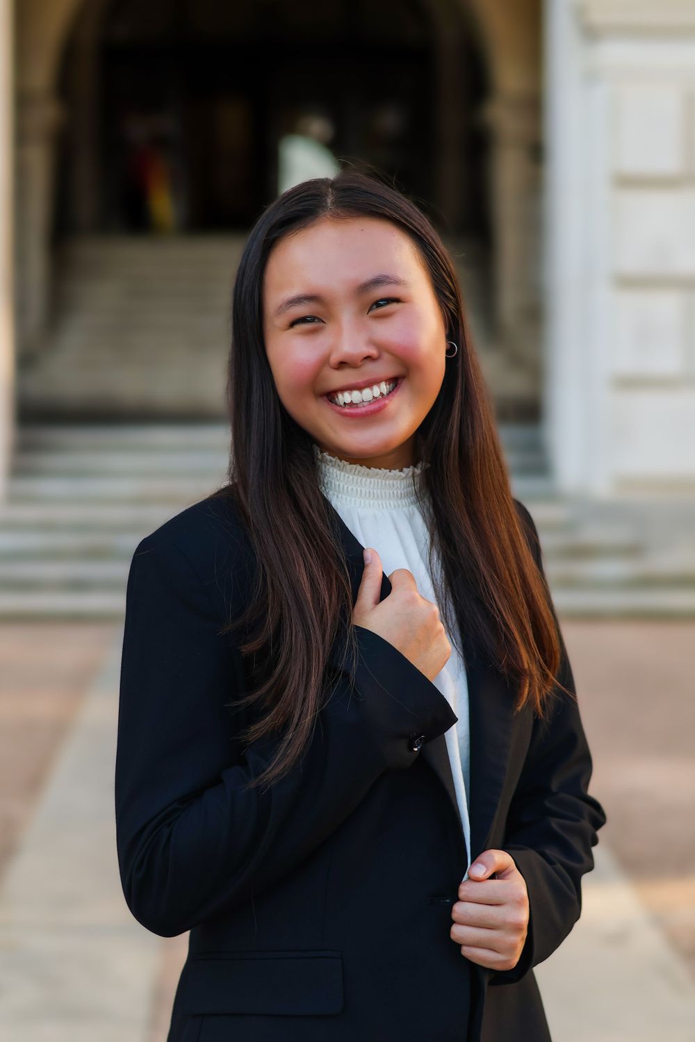 Professional portrait of businesswoman in black blazer and white sweater standing in archway.