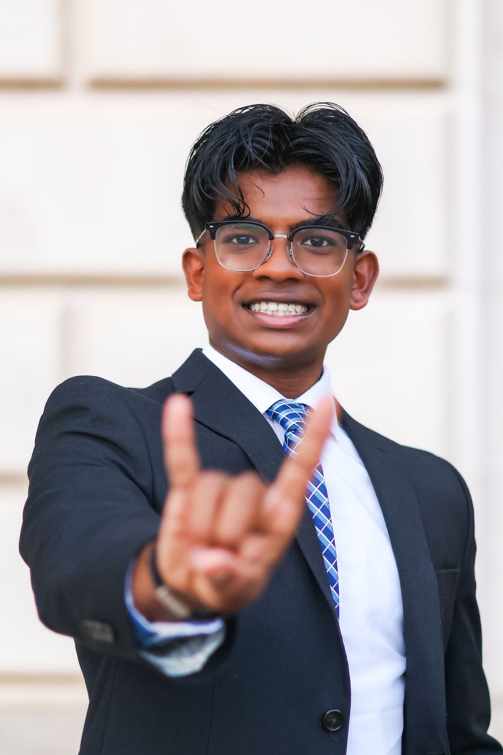 Professional in navy suit and blue striped tie making peace sign gesture against light background.