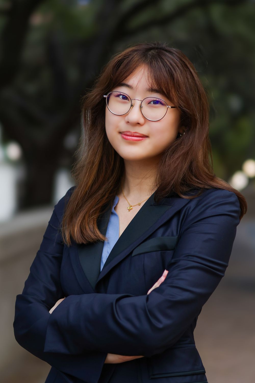 Professional wearing glasses and navy blazer poses confidently against blurred outdoor background.