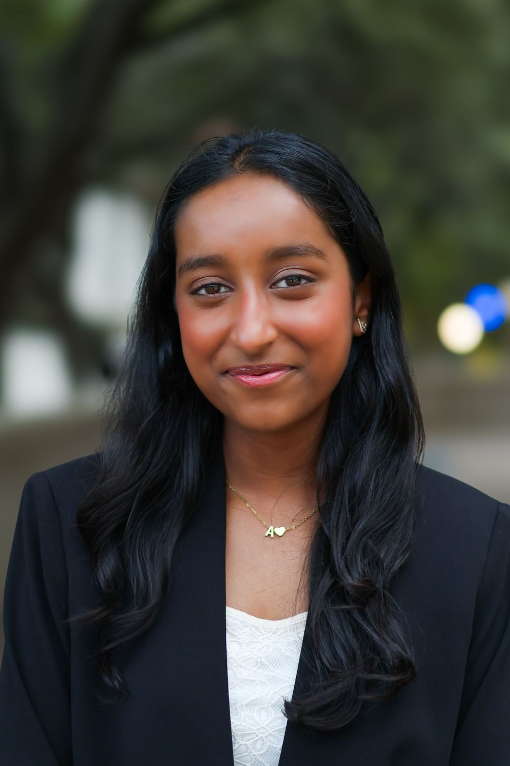 Professional in black blazer and white top smiling warmly in outdoor business portrait.