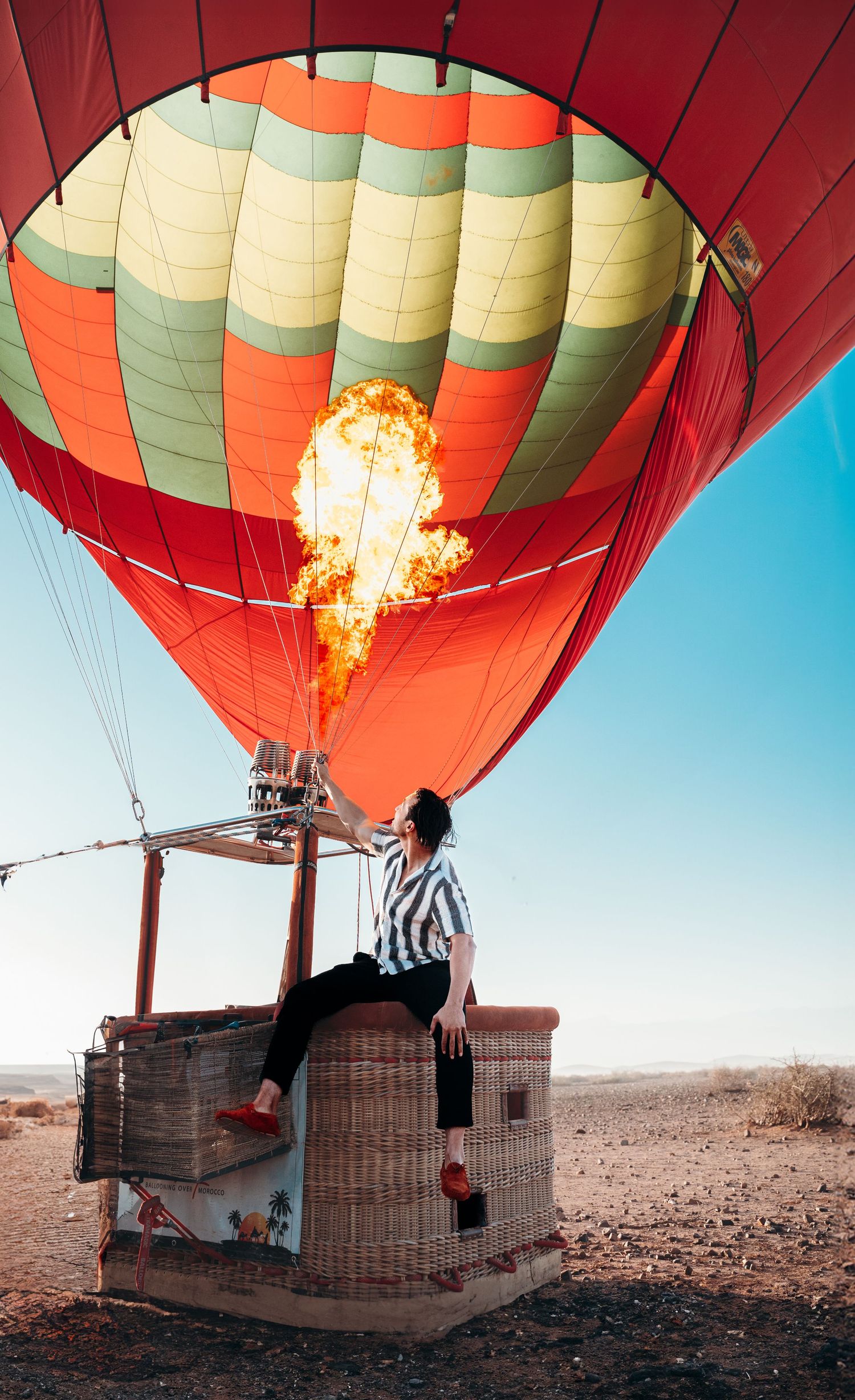 Hot air balloon with red and green stripes being heated for takeoff in a desert landscape.