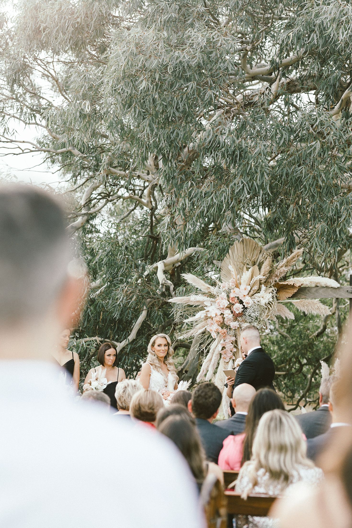 Outdoor wedding ceremony under cascading willow trees with dried floral arrangements.