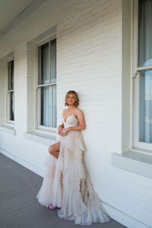 A flowing white wedding gown creates elegant contrast against a white colonial porch and windows.