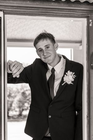 Black and white portrait of young man in suit and tie smiling at doorway.