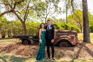 Formal couple poses in front of rustic vintage truck in outdoor setting with green foliage background.