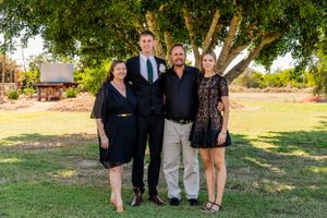 Small group poses together for formal outdoor family photo under large tree.