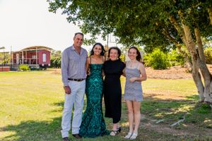 Small group in formal attire poses for photo on sunny grass lawn with buildings in background.