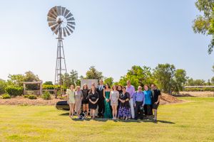 Large group poses together near rustic windmill in outdoor setting.
