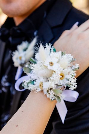 A delicate white floral corsage with ribbon tied around a wrist against formal black attire.