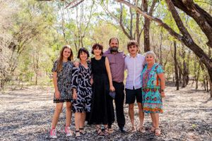 A family group poses together for a casual photo in a wooded outdoor setting.