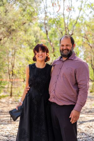 A sunny outdoor portrait of two people smiling together against a natural wooded background.