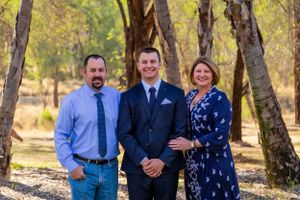 Three people pose for a casual outdoor portrait among autumn trees.