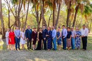 A large group gathers for a formal photo under palm trees in natural lighting.