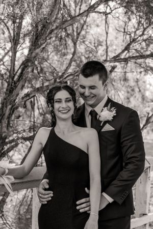 A couple shares a tender moment along a wooden fence in black and white photography.