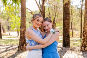 Two people embrace while wearing formal attire in a sunlit wooded setting.